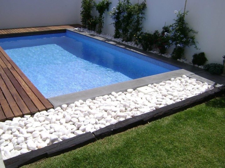 Piscina con borde de piedra blanca y madera.