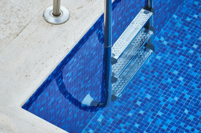 Esquina de una piscina en la que e aprecia el agua cristalina pues se ve la escalera a la perfección.